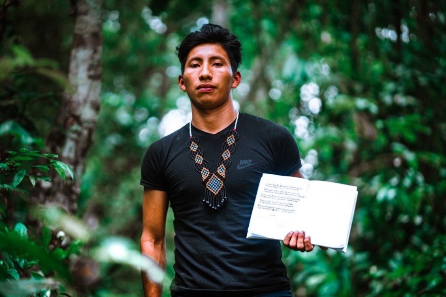 An Indigenous person from the Wampis Nation holding up a notebook with lyrics on it